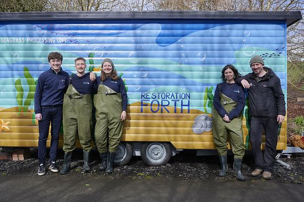 The Restoration Forth seagrass team stand in front of a tall trailer painted with images of sand, seagrass, oysters and the Restoration Forth Logo