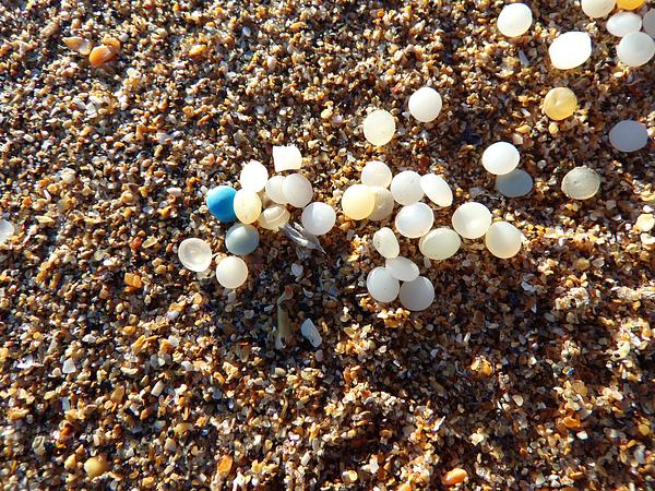 A bundle of tiny plastic pellets (nurdles) are scattered over sand