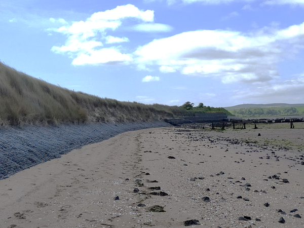 Wire mesh holds a slope of heavy stones in place in front of a sand dune that has been eroded Wire mesh holds a slope of heavy stones in place in front of a sand dune that has been eroded