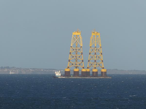 Two bright yellow structures (wind turbine foundations) tower out of a rough blue sea