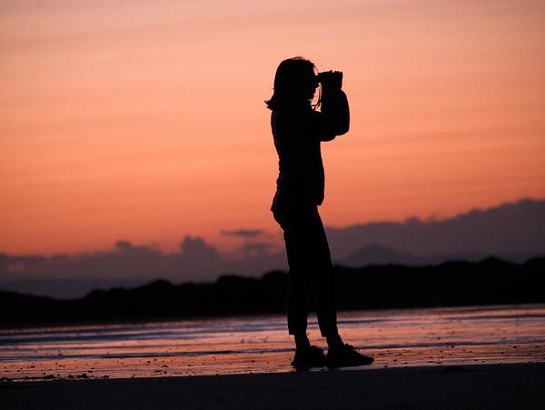 Person looking through binoculars as the sunsets
